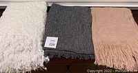 Three throws folded and placed side-by-side in white, gray, and dusty rose colors.