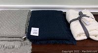 Gray, navy blue, and off white acrylic throws arranged side by side on hardwood floor