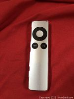 Front view of Apple Remote showing silver aluminum body with black circular control pad and MENU and play/pause buttons.