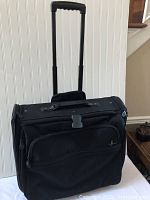 Overall view of the black Atlantic rolling luggage with extendable handle and front pockets.