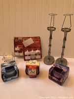 Photo shows battery-operated tea candle in glass holder, unopened GLADE scented candles (Invigorating, Sensual, Kiwi-Apple Crisp), and two silver metal candlesticks.