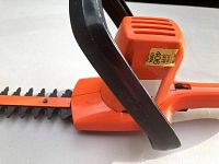 Close-up of orange Black & Decker electric hedge trimmer handle and blade, showing condition and sticker on motor cover.