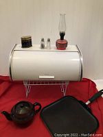 White Britannia bread box on stand, black ceramic teapot, griddle pan visible.