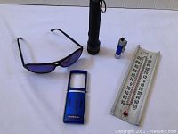 All items together on white background: Revo sunglasses, two flashlights (black and blue keychain), and Termarite thermometer.