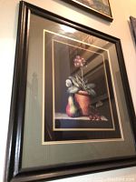 Front view of one framed print featuring a flower pot with flowers and assorted fruit in a black frame.