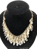 Close-up of goldtone necklace with clear glass teardrop beads displayed on black stand.