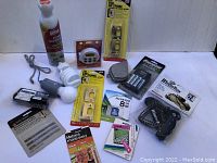 Photo of all household items including pest spray, timer, light bulbs, battery pack, Yaktrax grips, tape measure, light switch covers, SD card, and saw blades spread out on table