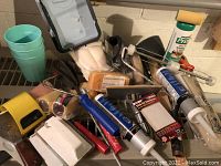 Overview of various paint accessories including roller frames, roller covers, caulk tubes, spreaders, sanding sponges and a yellow paint edger.