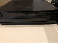 Front view of a black Kenwood multiple CD player with display and disc tray closed, showing play control buttons and disc selection numbers.