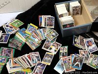 Large quantity of mixed baseball cards in and next to a shoebox, showing many cards stacked and spread out.