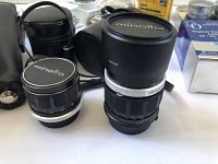 Close-up of two black Minolta camera lenses with lens caps on a surface