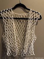 Front view of white pearl-like beaded vest hanging on black hanger against beige wall