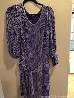 Front view of purple and white patterned Sister Max dress on hanger showing V-neckline, long sleeves, and attached waist belt.