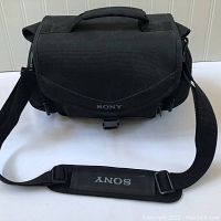 Front view of the Sony camera bag with shoulder strap laid flat showing the clasp and Sony logo on the flap and strap.