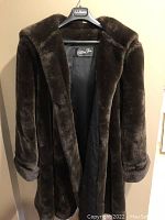 Front view of the dark brown faux fur coat on hanger, showing thick plush texture and shawl collar.