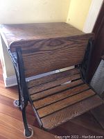 Side angled view of vintage oak schoolhouse desk showing wood grain, hinged top and cast iron leg.