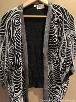 Front view showing black fabric with white and silver bead swirls and open front of jacket.