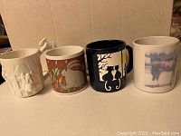 Photo of four animal themed coffee mugs including two with rabbit designs, one with cat silhouettes, and one with horse image.