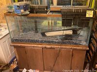 Glass aquarium filled with gravel set on wooden cabinet base with aquarium pumps and filters attached and aquarium lighting and accessories placed inside and around the aquarium.