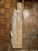 Two tightly rolled bamboo fencing rolls wrapped in plastic and tied, placed on parquet wood flooring.