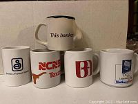 Photo showing five white ceramic coffee mugs with various vintage banking logos and branding, arranged in a row with one mug elevated in front center