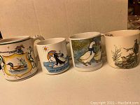 Four coffee mugs, each decorated with bird/fowl themes including duck, penguin, goose, and quail, arranged in a row.