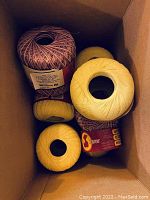 View inside box showing six large spools of embroidery thread in yellow and variegated pink-white colors.