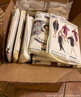 Box containing multiple vintage sewing patterns with visible Simplicity patterns including adult and children's clothing styles.