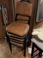 Five brown faux leather chairs stacked together, showing padded seats and backs and black metal frames.