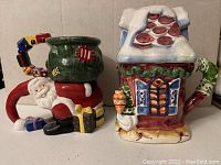 Photo showing two Christmas-themed ceramic mugs: a two-piece Santa stacking mug and a Christmas house mug with roof lid.