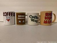 Photo of four coffee mugs lined up, each with a distinct printed design, showing fronts and handles.