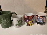 Photo of four floral and plant-themed coffee mugs arranged side by side showing different botanical designs and sizes.