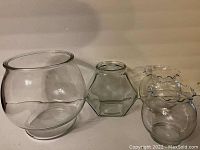 Four clear glass flower vases shown side by side on a neutral surface