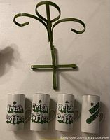 Set of 4 white Irish coffee mugs with green shamrock decorations and matching green metal countertop stand for hanging mugs.