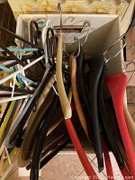 Box with assorted clothing hangers of plastic, wood, metal, and padded types in various colors and styles.