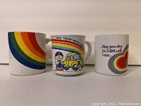 Photo showing three ceramic rainbow-themed coffee mugs with varying designs.