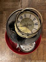 Top view of various clock parts including a Roman numeral clock face partly enclosed in a metal frame and additional clock faces beneath it