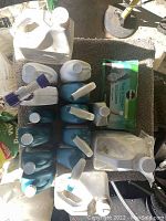 Multiple plastic gardening chemical containers arranged including large jugs and smaller spray bottles mostly white and teal color with screw caps and spray triggers