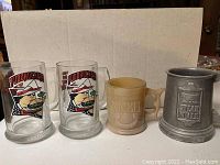 Four vintage restaurant mugs side by side: two clear glass Fuddruckers mugs, beige ceramic Whataburger mug, and metallic Steak N Ale mug.