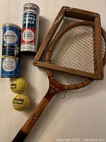 Vintage wooden tennis racquet with attached wooden frame holder, two metal tennis ball canisters labeled Spalding including some tennis balls visible outside them, all arranged flat on a surface.