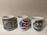 Three Washington DC souvenir coffee mugs showing colorful landmarks, patriotic design, and monuments.