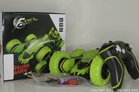 Photo of the Fancy Stunt Atom Max RC car with its box, remote control, and charging cable visible. The car is black with neon green accents and large tires.