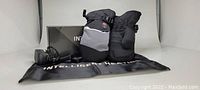 Photo shows a pair of rechargeable heated mittens in black and grey color with adjustable straps, charger, and black storage pouch labeled 'Intelligent Heated'.