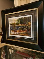 Framed print showing overall view with dark black frame and matting around the image of a canoe by the shoreline.
