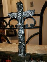 Front view of the small totem pole statue showing the bird with outstretched wings and multiple animal carvings stacked vertically on a rectangular base.