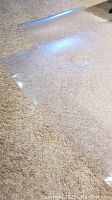 Clear rectangular plastic chair mat laid on beige carpet, showing transparency and slightly rounded corners.