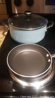 Large pastel blue pot with metal handles and transparent glass lid, sitting on stove.