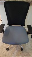 Front view of desk chair showing black mesh backrest and gray fabric seat with armrests and caster wheels.