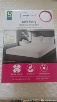 Front of box showing the Mainstays Queen Soft Terry Mattress Protector, highlighting features like bed bug resistant, waterproof, allergen barrier, and size fit.