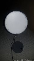 Straight-on view of the illuminated circular LED lamp head showing its smooth white diffuser surface.